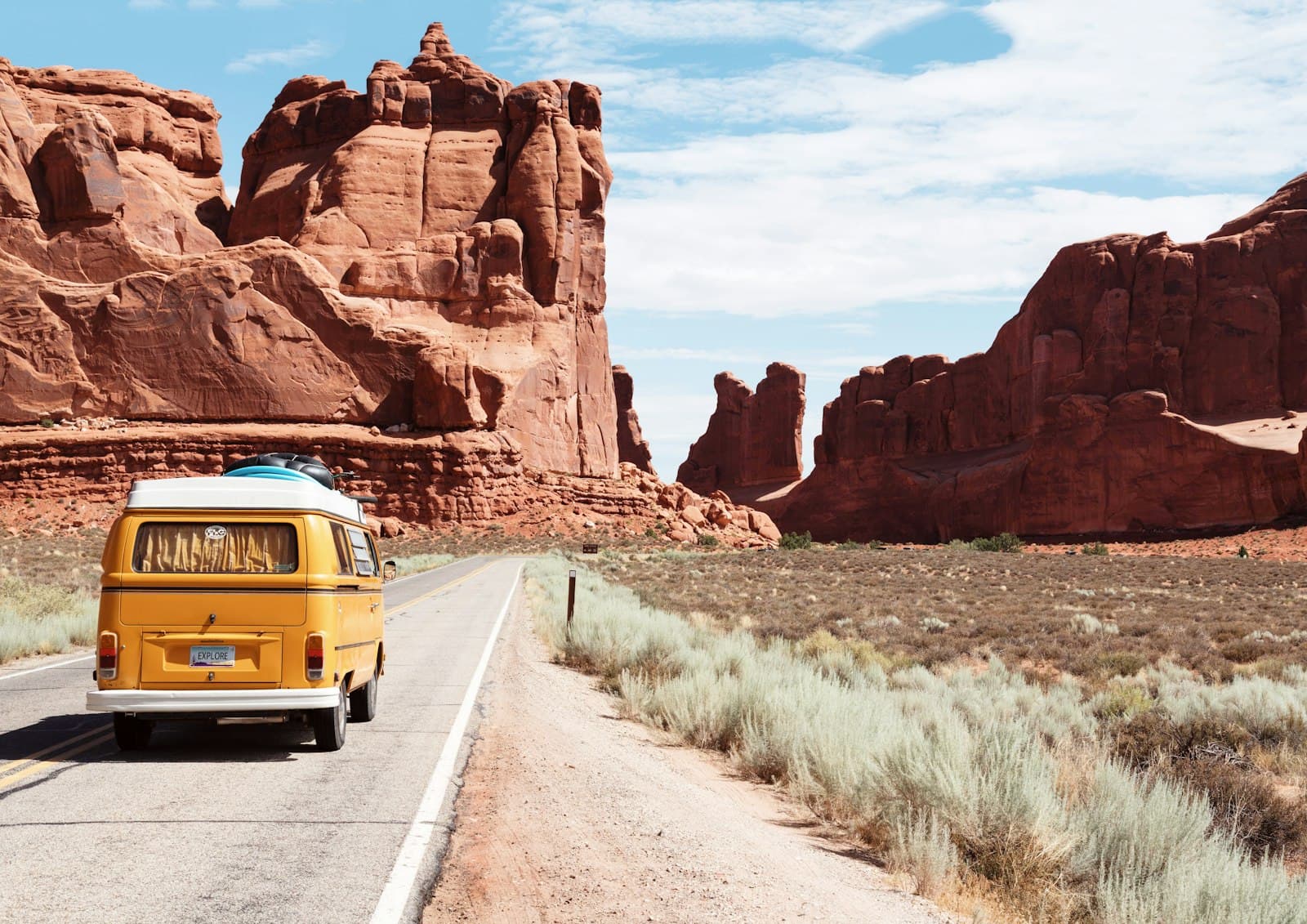 A yellow camper van on a paved road between red sandstone cliffs near Moab, Utah